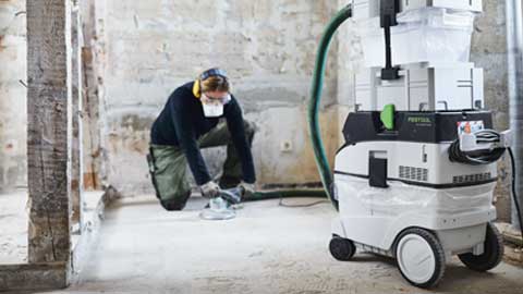 En håndværker sliber et gulv og bruger Festool gulvslibesystemet med støvsugning.
