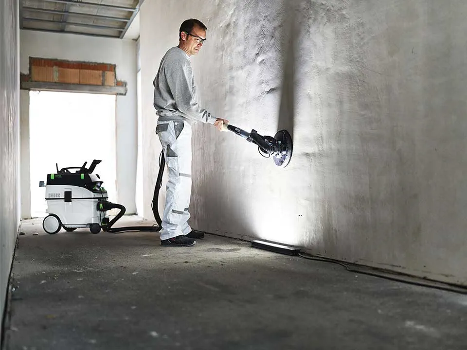 En håndværker belyser en væg ved hjælp af Kontrastlampen og sliber den ned