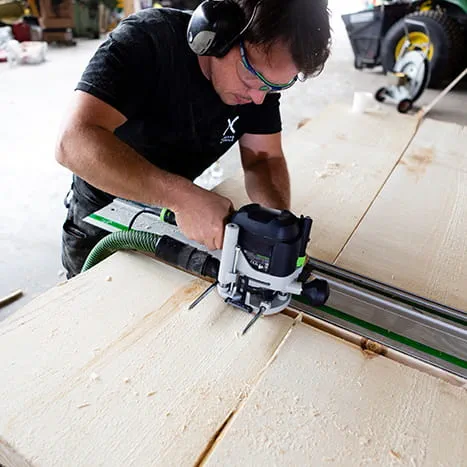 En saunabygger bearbejder en overflade med en overfræser fra Festool.