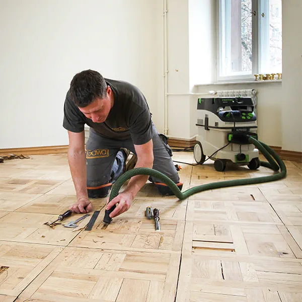 Parketgulvlæggermester Jarek Gawina løsner defekte dele fra parketgulvet og fjerner dem med Festool-støvsugeren